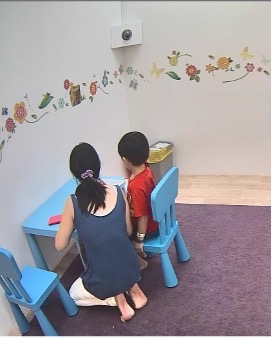 Back view of a parent and child seated together while completing the Etch-a-Sketch task; faces are not visible.